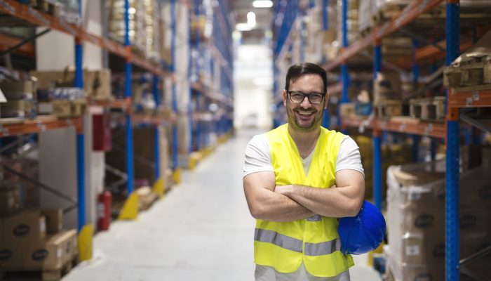 Portrait of middle aged warehouse worker standing in large warehouse distribution center with arms crossed.
